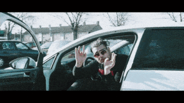 a man wearing sunglasses is sitting in a white car with his hands in the air