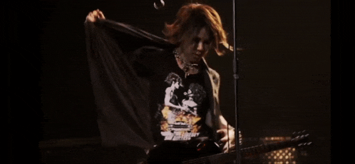 a man is playing a guitar and wearing a shirt that says " the greatest of all times "