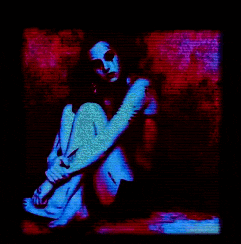 a woman is sitting on the floor in a dark room with a red and blue background