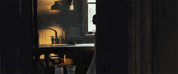 a person standing in a dark room with a sink and trash cans
