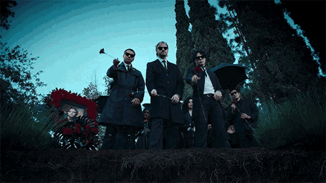 a group of men are standing in a cemetery holding umbrellas
