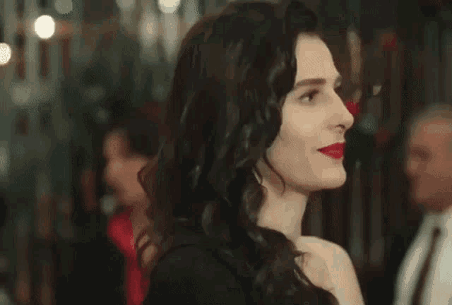 a woman in a black dress with red lips is standing in front of a crowd of people .