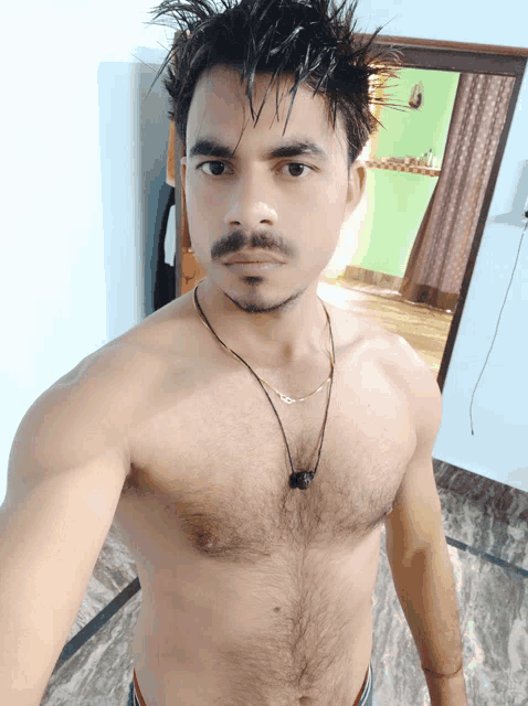 a shirtless man with a necklace around his neck takes a selfie