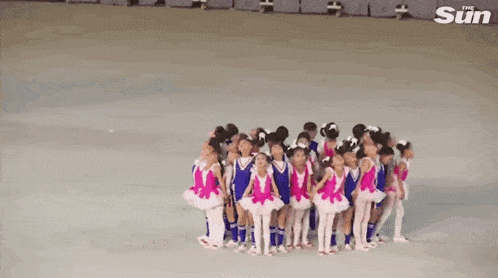 a group of children are dancing on a stage in front of the sun