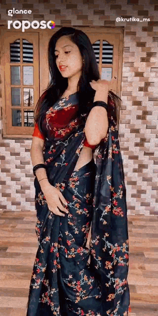 a woman in a black floral saree stands in front of a window
