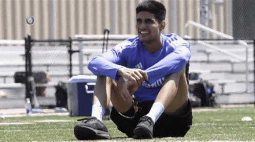 a man in a blue adidas shirt sits on a field