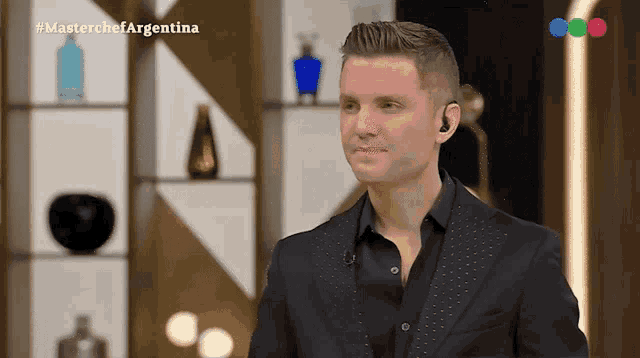 a man in a black suit is standing in front of a wall with bottles on it and the words masterchef argentina on the bottom