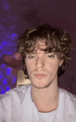 a young man with curly hair is wearing a nose ring