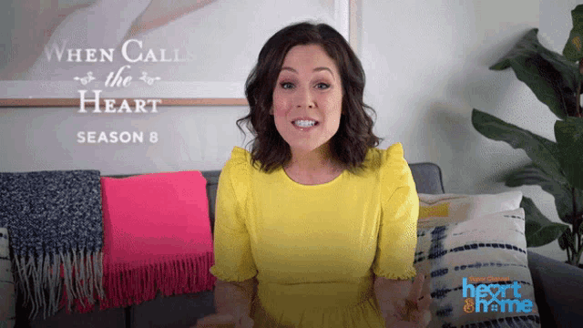 a woman in a yellow dress is talking in front of a sign that says " when calls the heart "