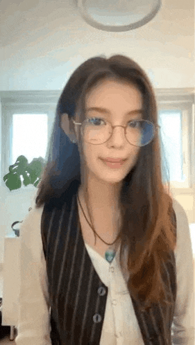 a woman wearing glasses , a vest , and a necklace is standing in a room .