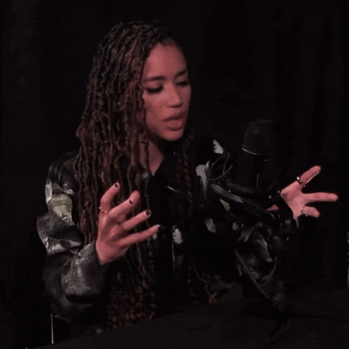 a woman with dreadlocks speaking into a microphone with her hands outstretched