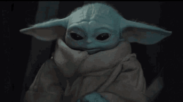 a baby yoda from star wars is holding a blue object .