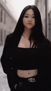 a woman wearing a black crop top and a black jacket is standing on a street .