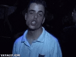 a man in a blue shirt is making a funny face with his mouth open in a dark room .