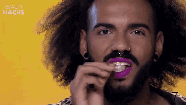 a man with curly hair and a beard is applying purple lipstick to his lips .