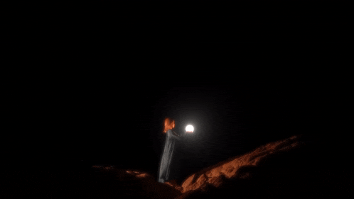a woman in a white dress is holding a light in her hand in the dark