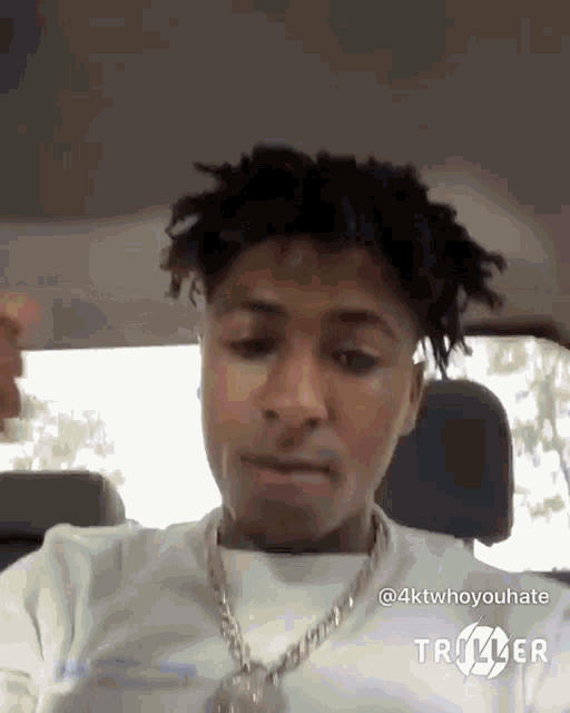 a young man is sitting in the back seat of a car wearing a chain around his neck .