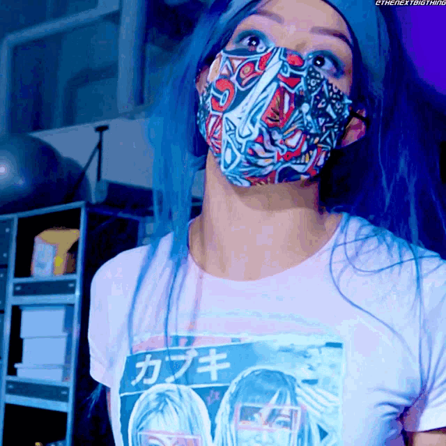 a woman with blue hair is wearing a face mask and a shirt that says the next thing