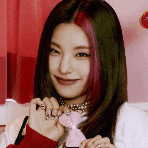 a woman with red and green hair is smiling and holding a pink bow