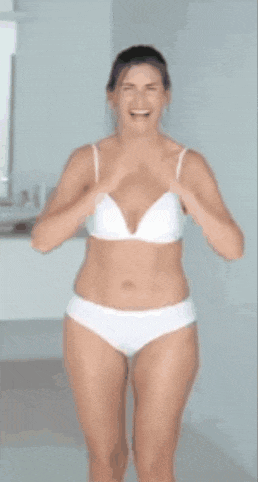 a woman in a white bra and underwear is standing in a bathroom and smiling .
