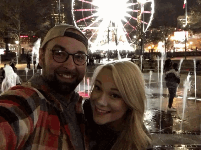 a man and a woman are posing for a photo in front of a ferris wheel