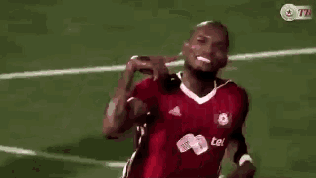 a man in a red jersey is standing on a soccer field with a soccer ball in the background .