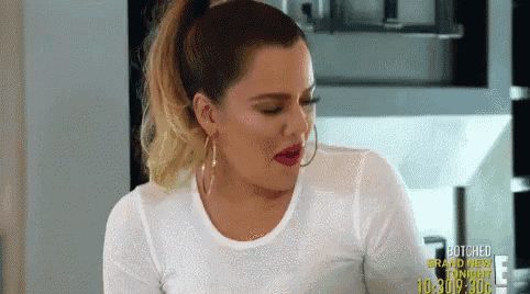 a woman in a white t-shirt and hoop earrings is sitting in a kitchen .