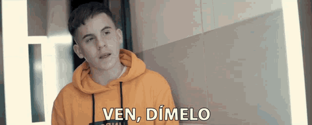 a young man in an orange hoodie says ven dimelo in spanish