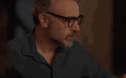 a man wearing glasses is drinking water from a glass .