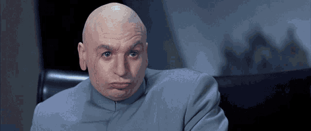 a bald man in a gray suit is making a silly face