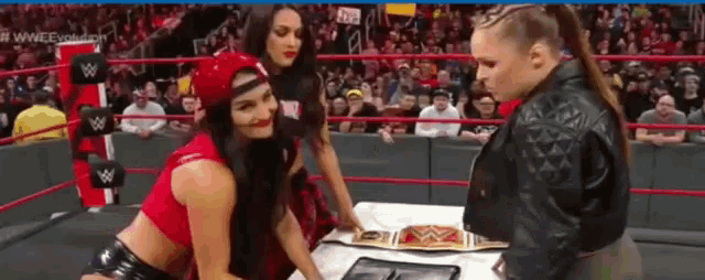 three women are wrestling in a wrestling ring and one of them is wearing a world heavyweight championship belt .