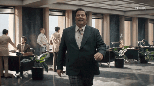 a man in a suit and tie walks through an office with the word max on the bottom right