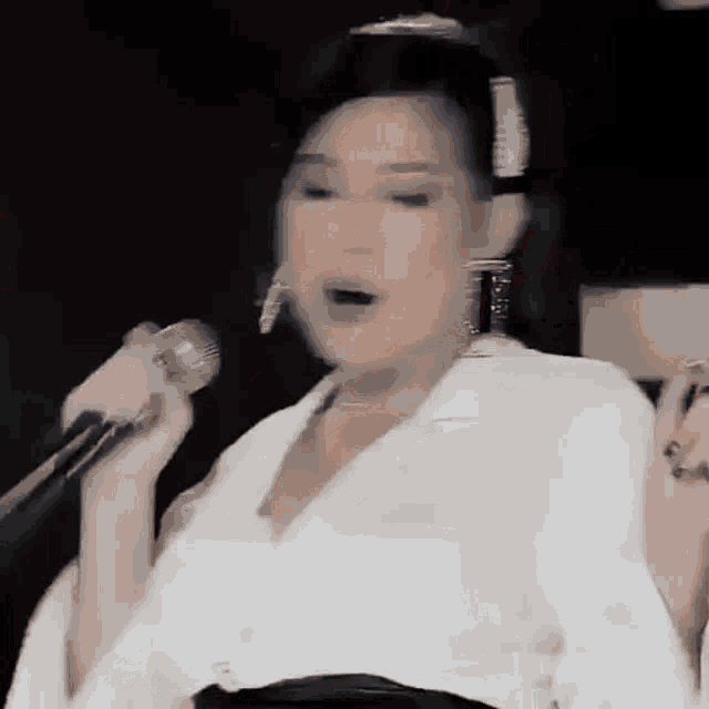 a woman is singing into a microphone while wearing a white shirt and earrings .
