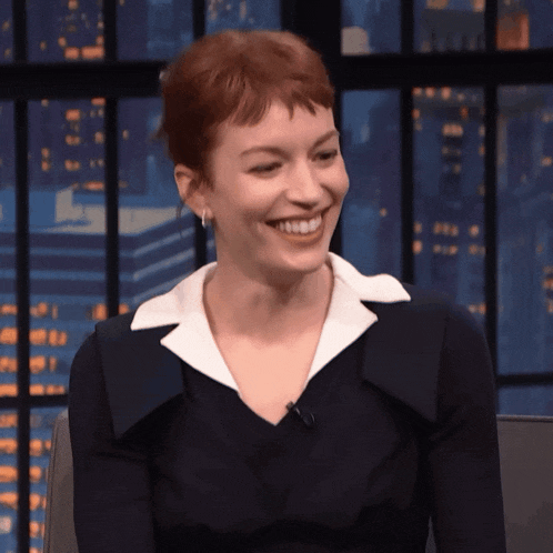 a woman with red hair is smiling while wearing a black dress and white collar