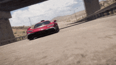 a red sports car is driving down a dirt road under a bridge