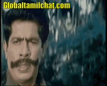 a man with a mustache is looking at the camera with the website globaltamilchat.com in the corner
