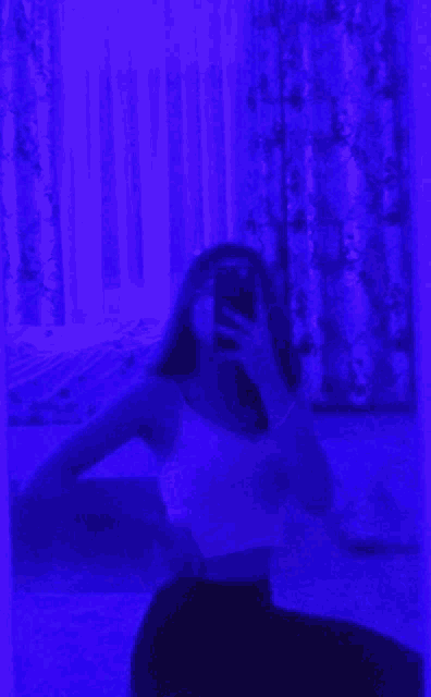 a girl is taking a selfie in front of a mirror with a purple light behind her .