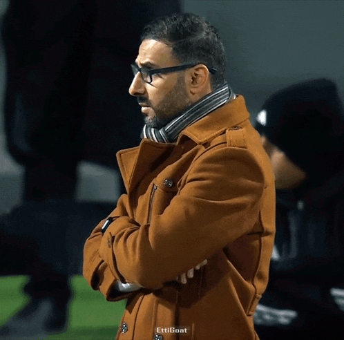 a man wearing glasses and a brown coat with the word ettigoat on the bottom right