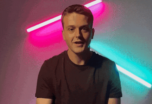 a man in a black shirt stands in front of a pink and blue light behind him