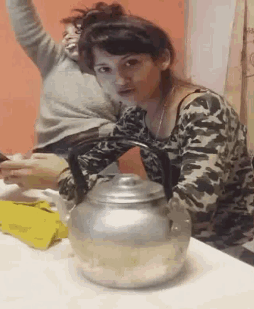 a woman in a camouflage shirt is holding a tea kettle on a table