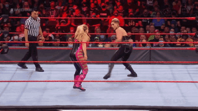two women are wrestling in a wrestling ring with a referee standing behind them .