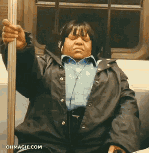 a woman wearing headphones is sitting on a subway and holding onto a pole
