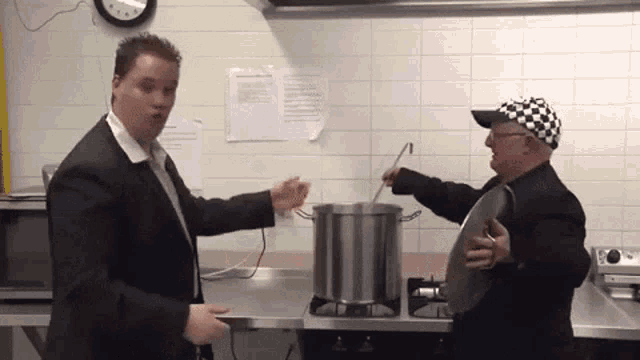two men are cooking in a kitchen with a clock on the wall above them