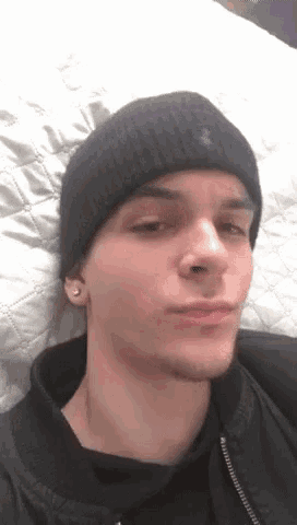 a young man wearing a black beanie and a black jacket laying on a bed