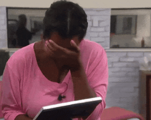 a woman in a pink shirt covering her face with her hands