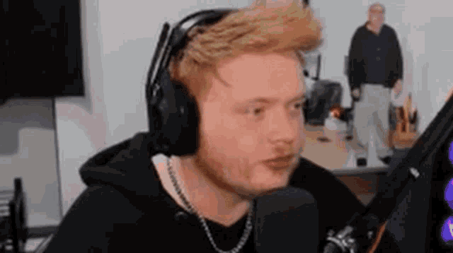a man with a beard is wearing headphones and a chain around his neck while talking into a microphone .