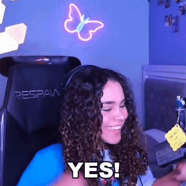 a woman with curly hair is sitting in a chair and smiling while holding a cell phone .