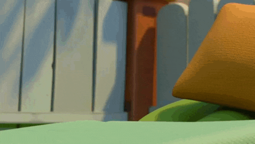 a green couch with a yellow pillow on it in front of a fence .