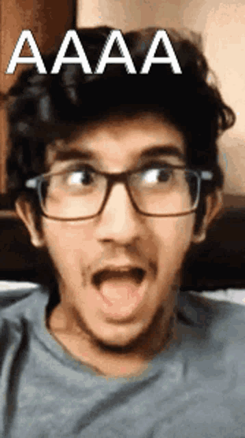 a man wearing glasses is making a funny face with his mouth open and the word aaa is above him .