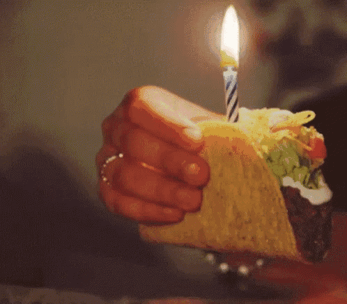 a person is holding a taco with a candle in it and the word ha is visible in the background